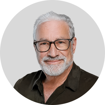 Portrait of a smiling older man with gray hair and beard wearing glasses and a dark collared shirt bioheadshot
