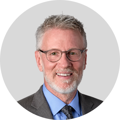 Smiling gray haired man wearing glasses and a suit in a professional head and shoulders portrait with a light gray background