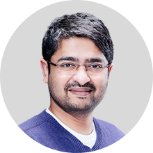 VivekM220 Hippocratic AI Hippocratic AI Smiling man with glasses and short dark hair wearing a purple sweater against a light gray background